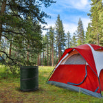 Green pop-up trash can placed next to a red and white camping tent in a forested campsite setting