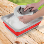 Hands washing a plate in a red and gray Wakeman collapsible wash bin filled with sudsy water
