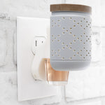 Plug-in wall diffuser shown inserted into outlet with a fragrance oil refill bottle attached beneath the diffuser