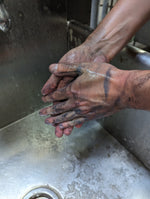Two dirty hands being rubbed together under running water in a stainless steel sink