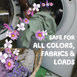 Hand placing laundry into a front-load washer with illustrated purple flowers and text saying safe for all colors, fabrics & loads