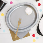 Gold plastic fork placed on a silver paper plate with confetti and napkins in a party table setting.