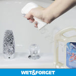 Hand holding a trigger sprayer directing foam at a bathtub faucet with a Wet & Forget jug partially visible at edge