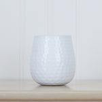 White hammered-texture oval iron planter placed on a light wood surface against a white paneled wall