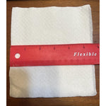 Folded white textured napkin on a wood surface with a red ruler laid across to show width