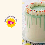 Tall decorated drip cake on a plate beside a badge reading 'Designed in the USA' against a light background