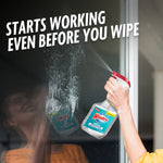 Hand spraying Windex with Vinegar onto a glass surface with visible spray and text saying it starts working even before you wipe