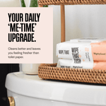 Stacked packs of Wipe That Tush flushable wipes arranged on a woven tray on a bathroom surface with a promotional headline.