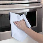 Hand using a white microfiber towel to wipe the front of a stainless oven door
