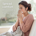 Woman seated on a sofa holding a tissue to her nose with overlay text urging to “Spread comfort this cold & flu season.”