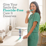 Woman in green pajamas brushing her teeth at a bathroom sink with a tube of Guru Nanda toothpaste on the counter.
