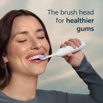 Woman smiling while using a Philips Sonicare electric toothbrush with text 'The brush head for healthier gums'