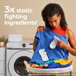 Woman inspecting clothing over a laundry basket with text highlighting '3x static fighting ingredients' and washer in background