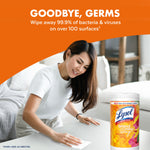 Woman wiping a table in a living room scene with a Lysol Brand New Day mango & hibiscus wipes tub shown at the corner