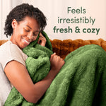 Woman cuddling a plush green blanket on a couch with overlay text feels irresistibly fresh & cozy