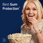 Smiling woman eating popcorn in front of a dark blue background with copy reading “Best Gum Protection” for Fixodent.