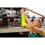Woman securing a bright yellow RESCUE! trap to a branch with a backyard barbecue scene softly out of focus behind her.