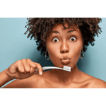 Woman holding a blue curved toothbrush near her mouth against a light blue background, surprised expression