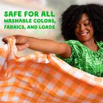 Smiling woman holding a checked orange sheet in front of laundry room backdrop with label safe for all washable colors and fabrics