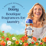 Smiling woman holding a Downy Citrea scent booster bottle in a floral meadow with text promoting boutique fragrances for laundry.