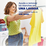 Woman holding up a bright yellow shirt in a laundry room with overlay text in Spanish and English about removing stains in one wash