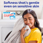 Woman hugging a plush blanket near a washer with product box inset and headline 'Softness that's gentle even on sensitive skin'.