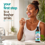 Woman smiling in bathroom setting holding a small cup while a GuruNanda oil pulling oral rinse bottle sits on the counter