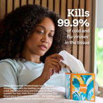 Woman pulling a tissue from a decorative Kleenex Anti‑Viral cube box with text claiming it kills 99.9% of cold and flu viruses.