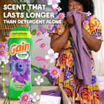 Woman smelling a purple garment beside a large Gain Moonlight Breeze bottle with text claiming longer lasting scent