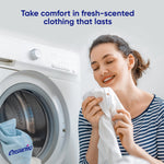 Woman holding and smelling a freshly laundered shirt next to a front-loading washer and an Ensueño laundry bag