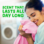 Woman smiling and inhaling freshly laundered pink fabric with a washer blurred in the background