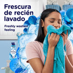 Woman smelling a turquoise towel with a Downy Intense bottle and blue floral splash artwork in the background