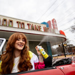 Smiling woman in a convertible spraying a Citrus Magic Limoncello car spray with mist visible