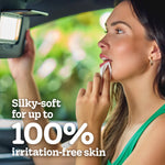 Woman using a tissue at her mouth while looking into a car visor mirror with text claiming 'silky-soft for up to 100% irritation-free skin'
