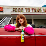 Woman leaning on red convertible door holding a Citrus Magic Limoncello car spray can in front of a diner
