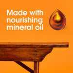 Wood table edge with an oil droplet graphic and text ‘Made with nourishing mineral oil’ on orange background