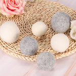 Wool dryer balls in white and gray arranged in a woven basket with decorative flowers beside them.