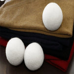 Three white wool dryer balls displayed on folded sweaters to suggest laundry use