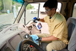 Person wearing gloves and safety glasses wiping a truck dashboard while holding a GUNK spray bottle