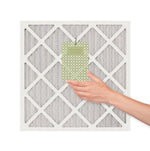 Hand placing a green Yankee Candle hanging air freshener onto a furnace/AC filter grid, white background.