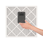 Hand attaching a small rectangular Yankee Candle scented device to a furnace or A/C filter shown against a white filter grid