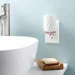 White textured Yankee Candle ScentPlug diffuser plugged into a wall outlet beside a bathroom sink and soap dish.