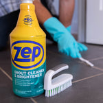 Zep grout cleaner bottle in foreground with scrubbing brush and gloved person cleaning tile grout in background