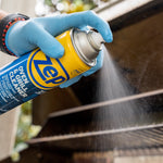 Gloved hand spraying a fine mist from a Zep oven & grill cleaner can onto an outdoor grill grate.