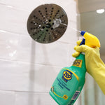 Gloved hand spraying Zep Home Pro foaming bathroom cleaner toward a showerhead and tiled wall
