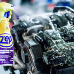 Close-up of a gloved hand holding a Zep spray bottle foaming cleaner on a greasy engine in a workshop setting