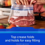Clear Ziploc freezer bag holding raw meat on a countertop with hands above and caption 'Top crease folds and holds for easy filling'