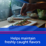 Hand seasoning a piece of fish on a cutting board with a Ziploc freezer bag and ingredients in background